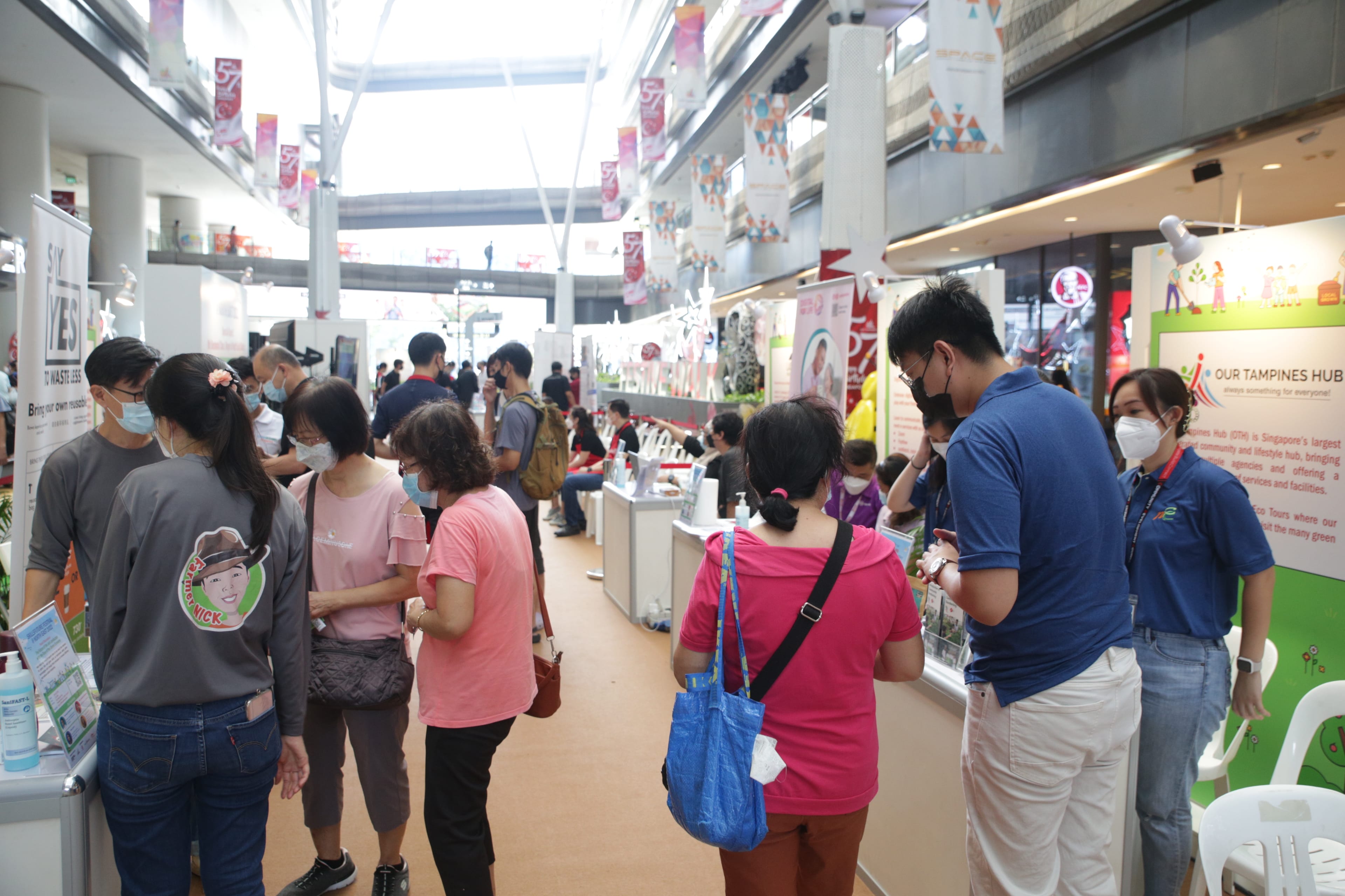 Several people are standing and talking in a bright indoor exhibition space with various booths and informational displays.